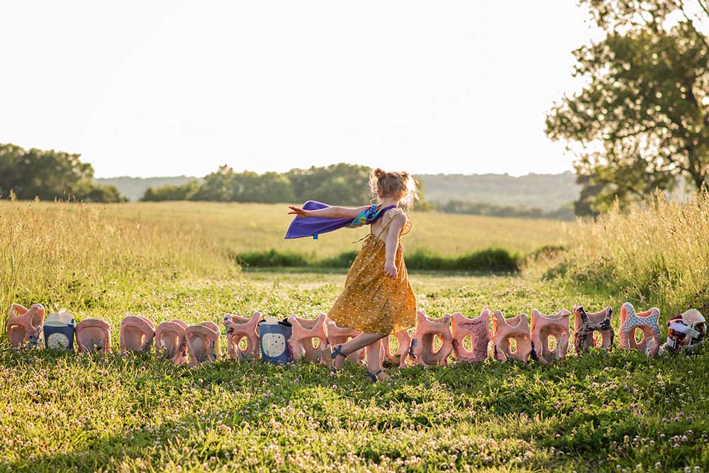 Quinn Liberman with a cape around her neck running alongside a row of back braces in a grassy field