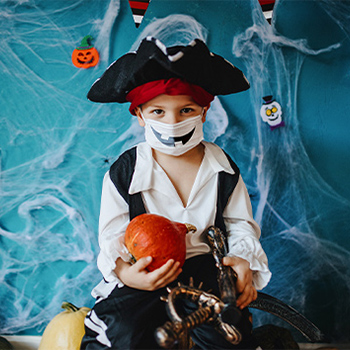 A child dressed as a pirate for Halloween with a white face mask that has black jack-o-lantern teeth