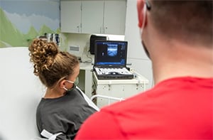 A young patient and a Children's Mercy nurse looking at the ultrasound of the patient's veins on a small computer screen.
