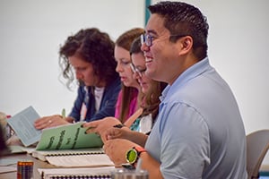 Group of four people sitting at a table with booklets in front of them smiling.