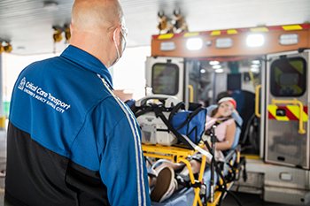 Critical Care Transport member helping load a patient on a gurney into an ambulance.