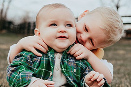 Color photo of Will McKinnon and his brother, Ben. Ben is sitting behind Will with his hands on his shoulders smiling.