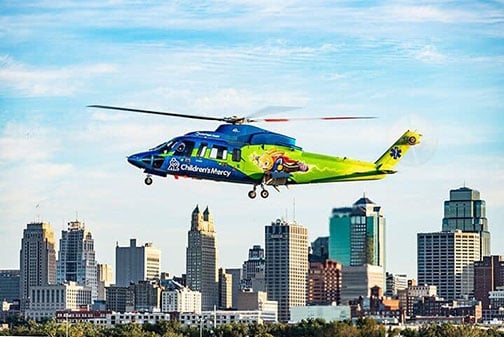 Children's Mercy Critical Transport helicopter in the air with the Kanas City skyline in the background.