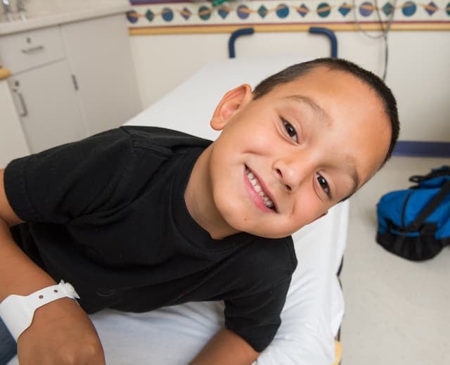 Child on an exam table in a clinic setting wearing a hospital wristband.
