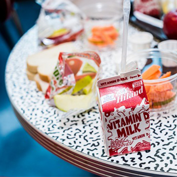 A small milk carton with a straw, bread slices, apples slices, and carrot sticks on a table.