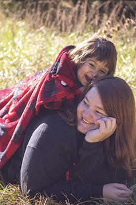 Cambree Alvarez laying on her mom's back outside, both are smiling.