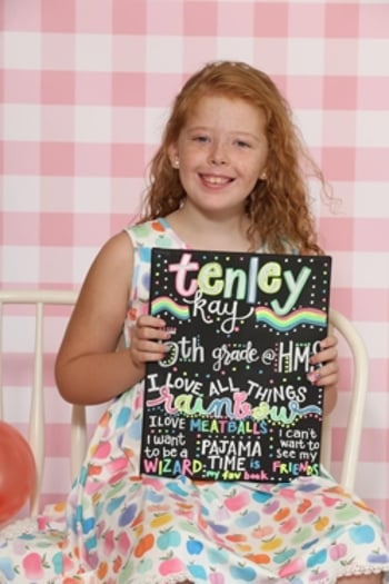 Tenley, a smiling child with red hair holding a first day of school sign