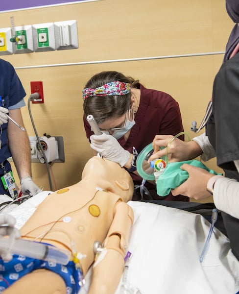 A masked woman practices intubation on a medical simulation mannequin.
