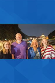 Four members of the Onley famliy smiling outdoors at night with a building in the background.