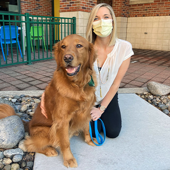 Hunter with handler Aimee Hoflander. Aimee is wearing a face mask and kneeling outside Children's Mercy with Hunter by her side.
