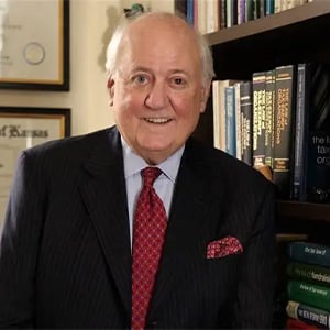 Bruce Hopkins smiling in front of a wall with framed licenses and a filled bookshelf.