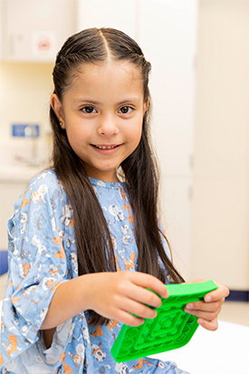 Girl in hospital gown smiling and playing with a toy at Children's Mercy.