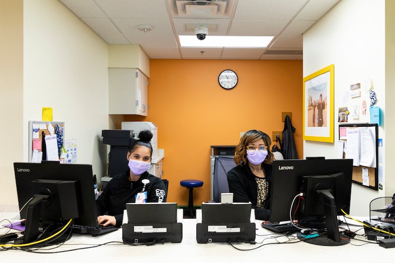 Two women sitting at computers check in patients at the Children's Mercy Genetics clinic.