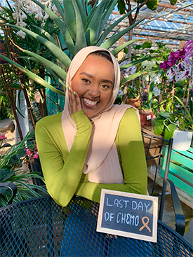 Munira  Nuru smiling and sitting in back of a sign that reads, "Last day of chemo."