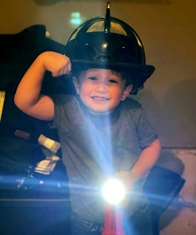 Paxton Koehler smiling and wearing a firefighter's hat. He has a flashlight in his left hand and showing off his bicep with his right arm.