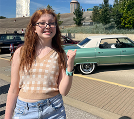 Lacie outside at Gateway Arch National Park. She is smiling and pointing over her shoulder at a green classic car.