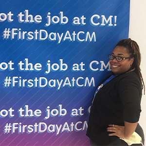 Yalanda Jackson smiling at a Children's Mercy employee orientation. She is standing in front of a sign that repeats the words, "I got the job at CM! #FirstDayAtCM."