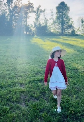 ella in a dress and hat outside in the grass 