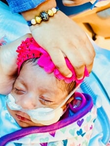 Sleeping infant with pink bow and brother's hand on her head showing the rakhi, thread of love, wrapped around his wrist.
