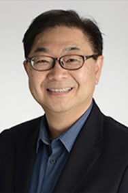 Dr. Tomoo Iwakuma smiling in front of a light colored background.