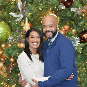 Brandy Dillingham hugging her husband and smiling in front of a decorated Christmas tree.