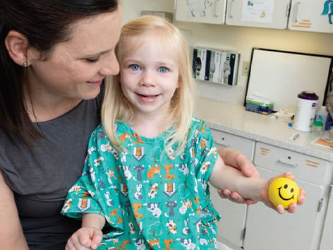 Child sitting in mother's lap while holding a smiley face stress ball.