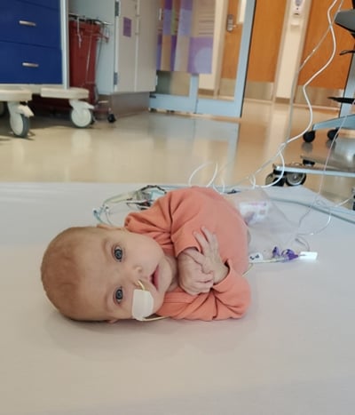 An image of a baby girl on the floor with a tube in her nose and other medical equipment nearby.