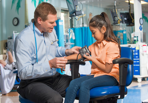 A male doctor measures a young girl's blood pressure using a blood pressure cuff and stethoscope.