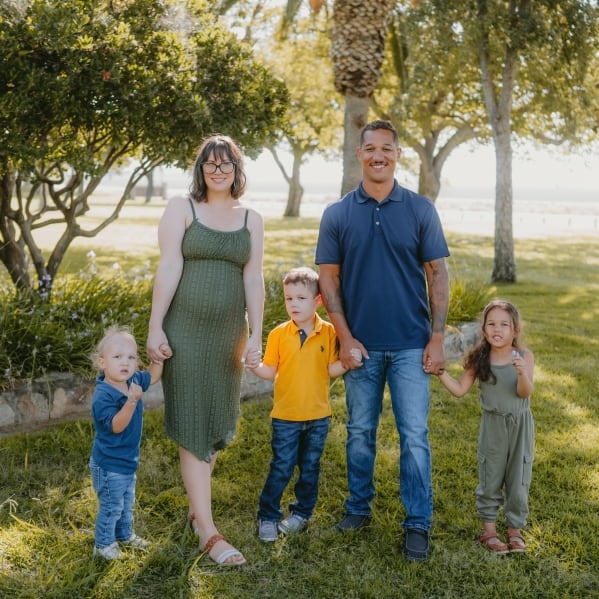 A woman in a green dress and a man in a blue shirt hold hands with 3 young children in a family portrait.