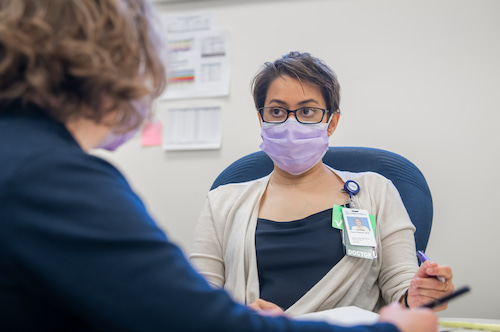 A woman wearing a surgical mask talks with another woman one-on-one.