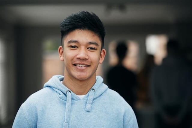 A teenage boy wearing a blue hoodie looks directly at the camera with a slight smile.