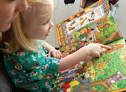 Mother using an I Spy book to distract her child before a needle procedure.