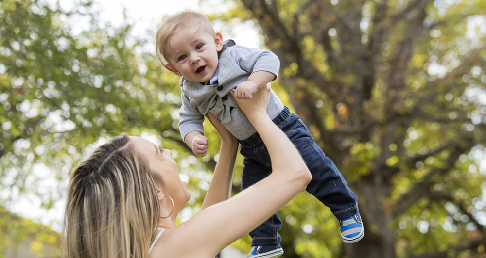 Holden smiling while his mother holds him in the air