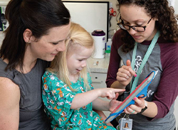 Mother and nurse using tablet device to distract a child before a needle procedure.
