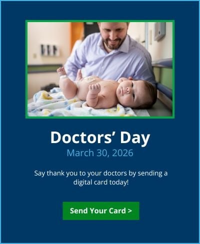 A baby in a diaper lies on a medical exam table while a man with a purple shirt looks down at him. Text reads: Doctors' Day, March 30, 2026. Say thank you to your doctors by sending a digital card today! Green button reads Send Your Card.