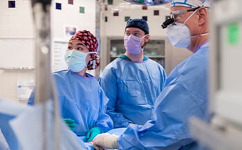 Two surgery fellows assisting in a surgery with a Children's Mercy doctor. All are wearing surgical items, including face masks, surgery caps, gowns, and gloves.