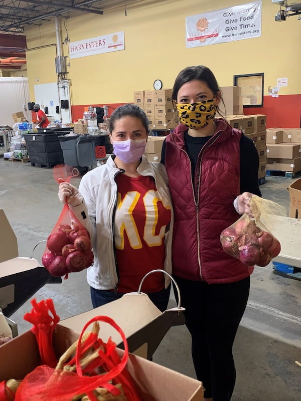 Two masked young adult women hold bags of onions at a food pantry.