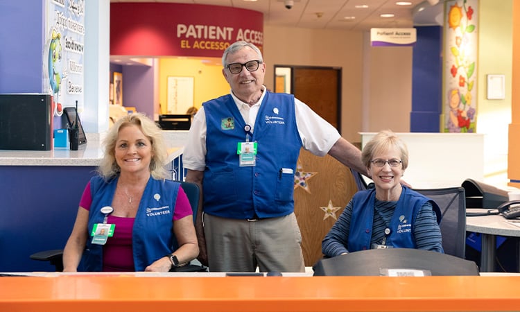 Three Children's Mercy volunteers smiling behind the Guest Services desk at Children's Mercy Adele Hall.