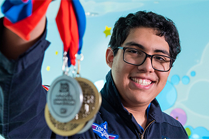 Teo smiling and holding up multiple medals.