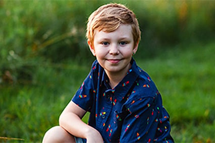 Austin Hasenohr grinning and kneeling outside in a field of grass.