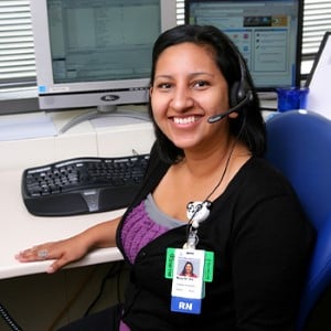 Children's Mercy nurse (RN) sitting in front two computer screens and a keyboard. She is smiling and wearing a headset.