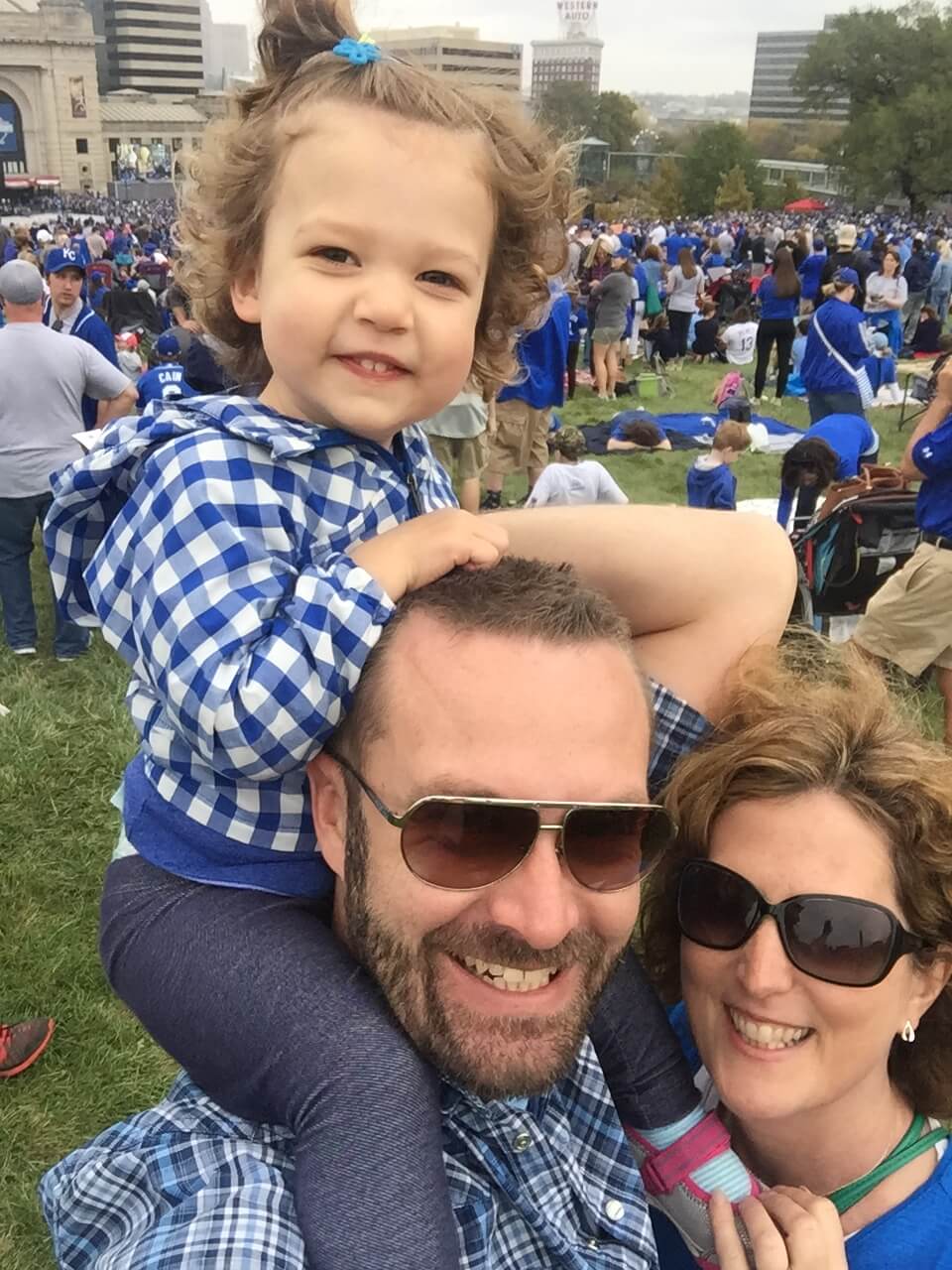 Ainsley smiling with her dad and mom (Ainsley is sitting on her dad's shoulders)