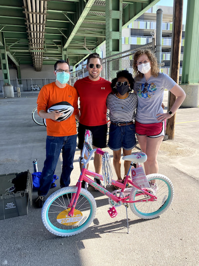 Four young people, some of them masked, standing outdoors near a new girls' bike.