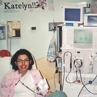 A young patient sits in a hospital chair connected to a dialysis machine, with medical equipment visible beside the bed.