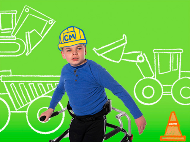 Boy with a walker wearing an illustrated construction hard hat with illustrated construction vehicles in the background.