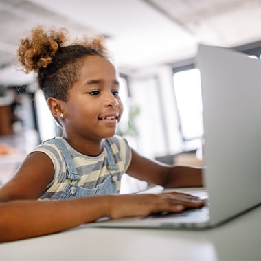 Child look at a laptop smiling and pressing button on the keyboard.