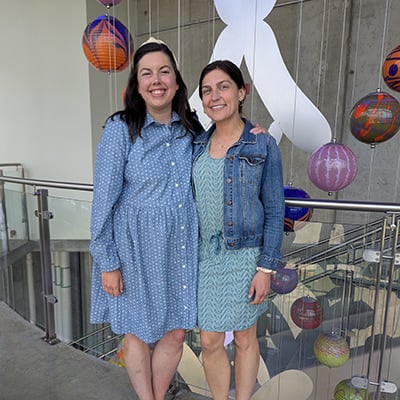 Two adults stand arm in arm at Children’s Mercy, with suspended glass sculptures visible in the background.