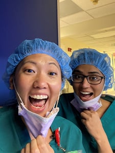 Two GI fellows in scrubs and scrub caps pulling down their face masks and smiling