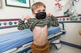Tripp Chase holding his shirt up in a Children's Mercy patient room to show his kidney removal scar (lower right abdomen).