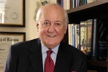 Bruce Hopkins smiling in front of a wall with framed licenses and a filled bookshelf.